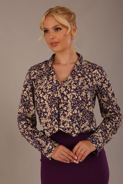 Woman wearing a floral blouse with a plain background: The Truro top's unique draped V-neck with its two elegant front ties. Close-up view