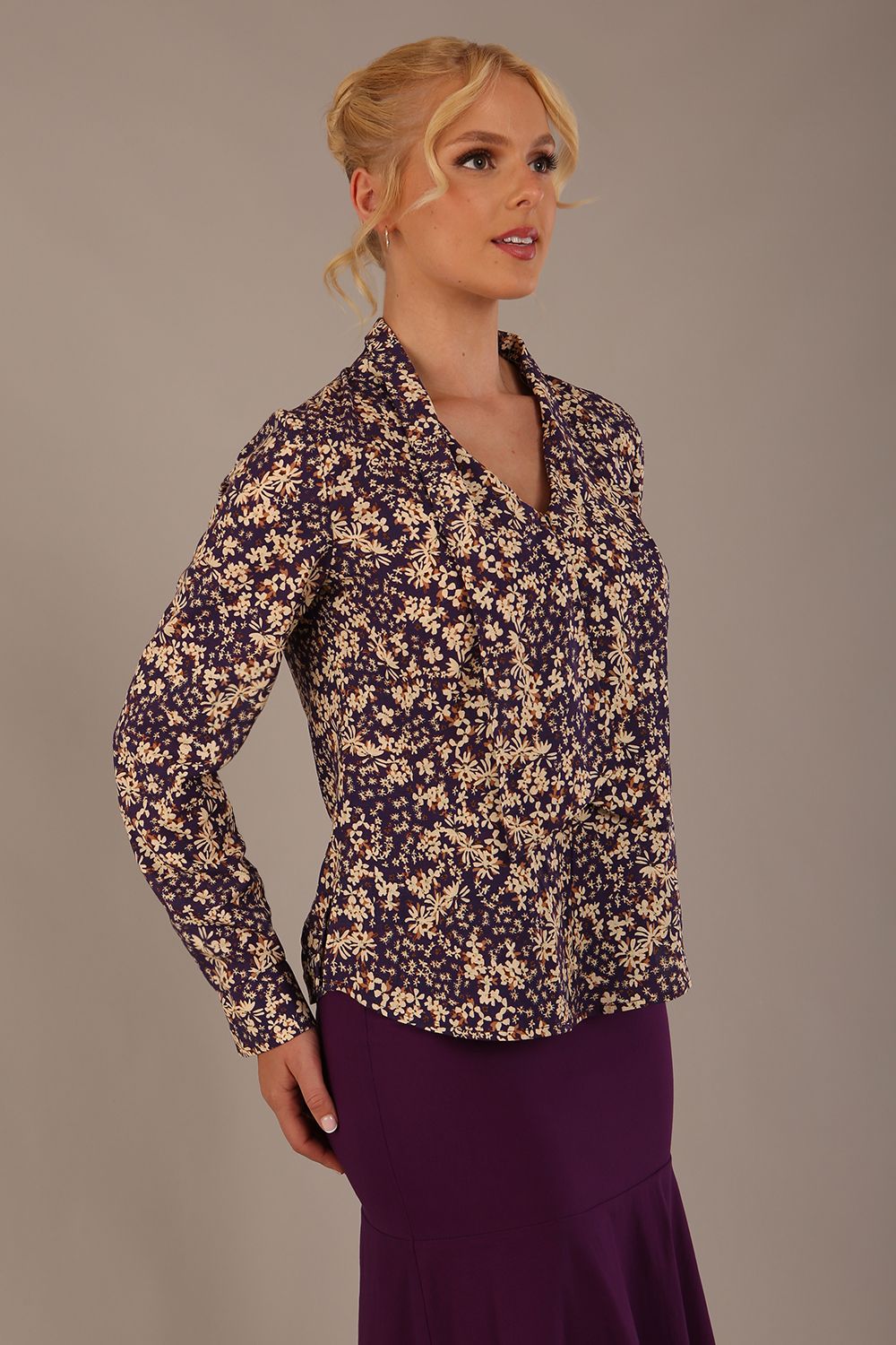 Model wearing the Truro floral top, showing the standard hip-length and draped V-neck and purple skirt against a beige background side view