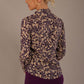 Model wearing the Truro floral top, showing the standard hip-length and draped V-neck and purple skirt against a beige background back view