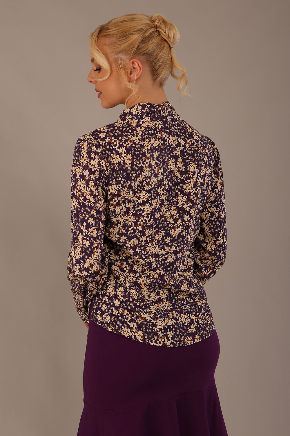 Model wearing the Truro floral top, showing the standard hip-length and draped V-neck and purple skirt against a beige background back view