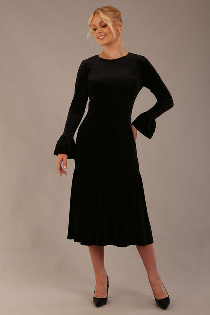 Model wearing the Sophisticat fluted sleeve velvet dress in black.