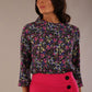 Woman wearing a floral top and pink skirt with black buttons against a neutral background