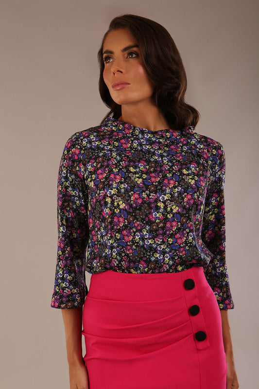 Woman wearing a floral top and pink skirt with black buttons against a neutral background