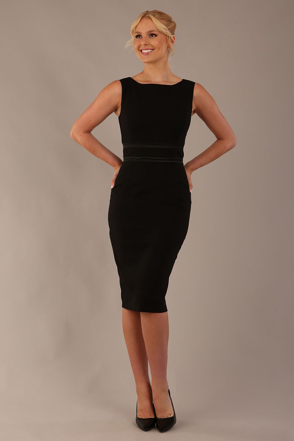 Model wearing the Rialto sleeveless pencil dress in black, showing the boat neckline and satin waistband.
