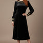 Woman wearing a black dress with long sleeves on a beige background  (Black Velvet with Sherwood Glitter Contrast)