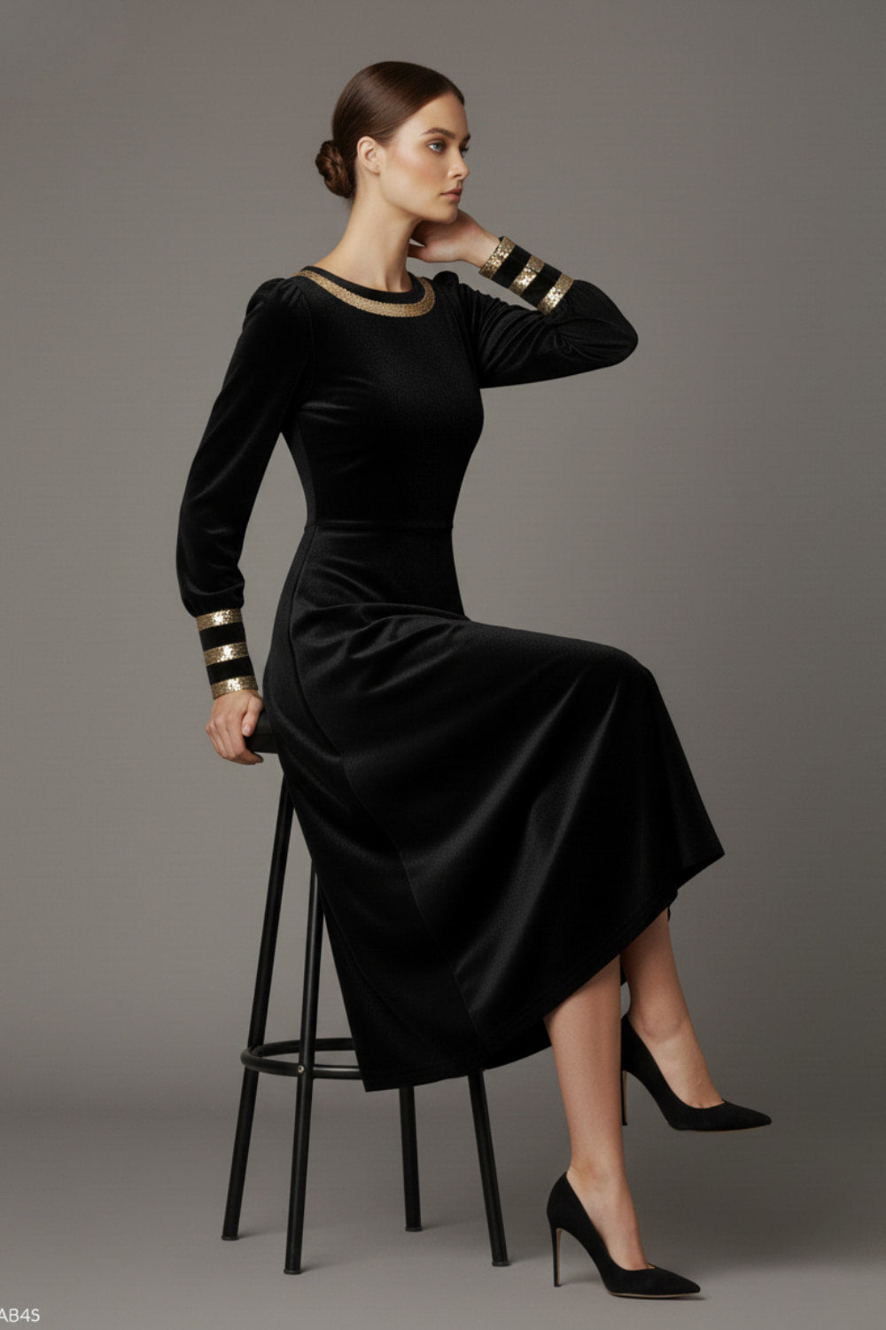 Model sitting wearing the diva catwalk Spinetti long-sleeved jewelled velvet midi dress in black.