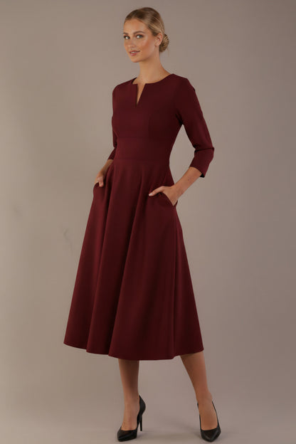 Model wearing the Perpetua A-line dress in wine with hands in pockets (Wine)