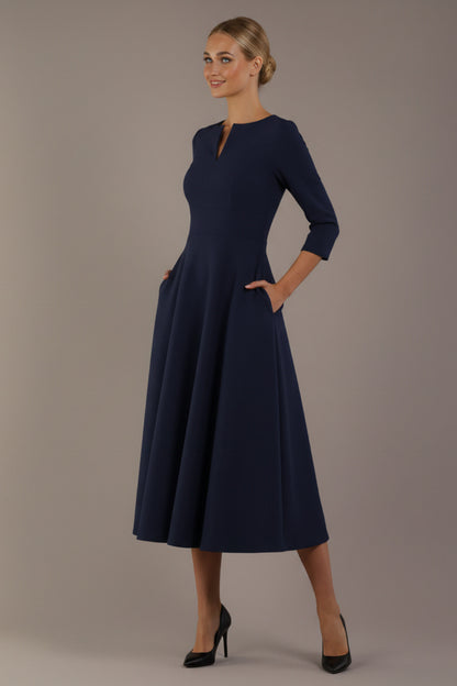 Model wearing the Perpetua A-line dress in navy blue with hands in pockets (Navy Blue)