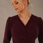 Model wearing the Calvert sparkle A-line dress in burgundy, showing the wrap V-neckline highlighting the fluid A-line skirt and long sleeves, Close-up of the shimmering sparkle stretch fabric and V-neck bodice on the Calvert dress (Burgundy Sparkle)