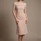 Woman wearing a diva catwalk Francesca Lace Fluted Dress in pink haze colour dress with lace sleeves against a brown background front view (Pink Haze)