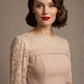 Woman wearing a diva catwalk Francesca Lace Fluted Dress in pink haze colour dress with lace sleeves against a brown background front close up (Pink Haze)