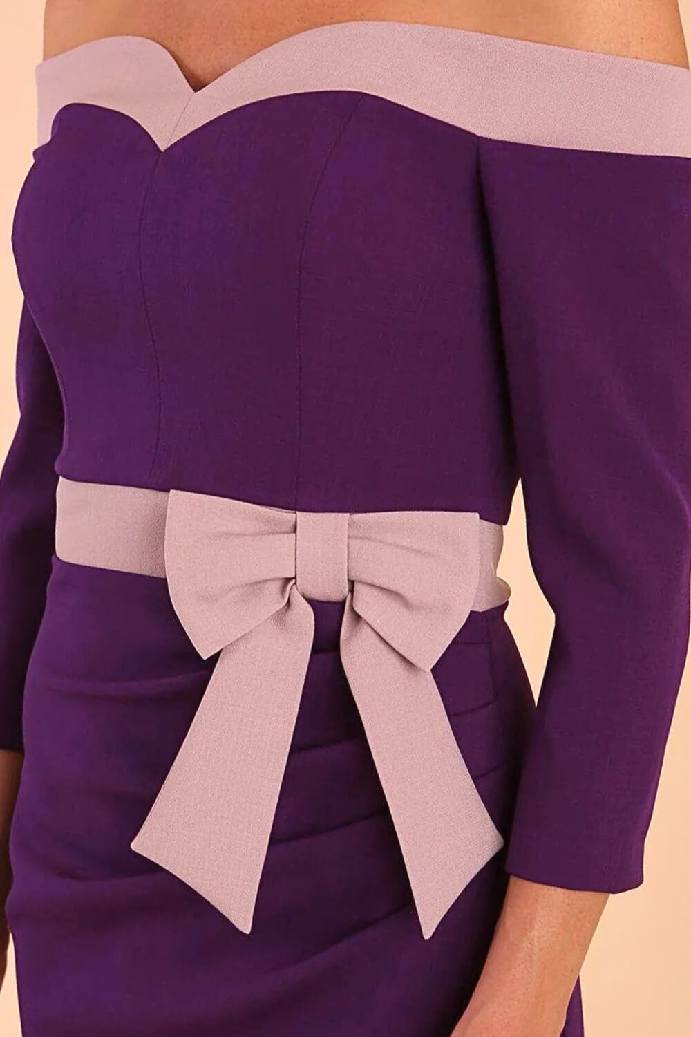 Model wearing a diva catwalk Brittany Off Shoulder Bow detail Pencil Dress with 3/4 sleeves and knee length in Deep Purple and Thunder Bird colour bow side detail
