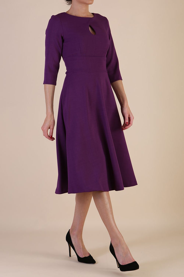 Brunette model is wearing diva catwalk casares swing dress with a keyhole neckline three quarter sleeve dress with pocket detail in imperial purple side front