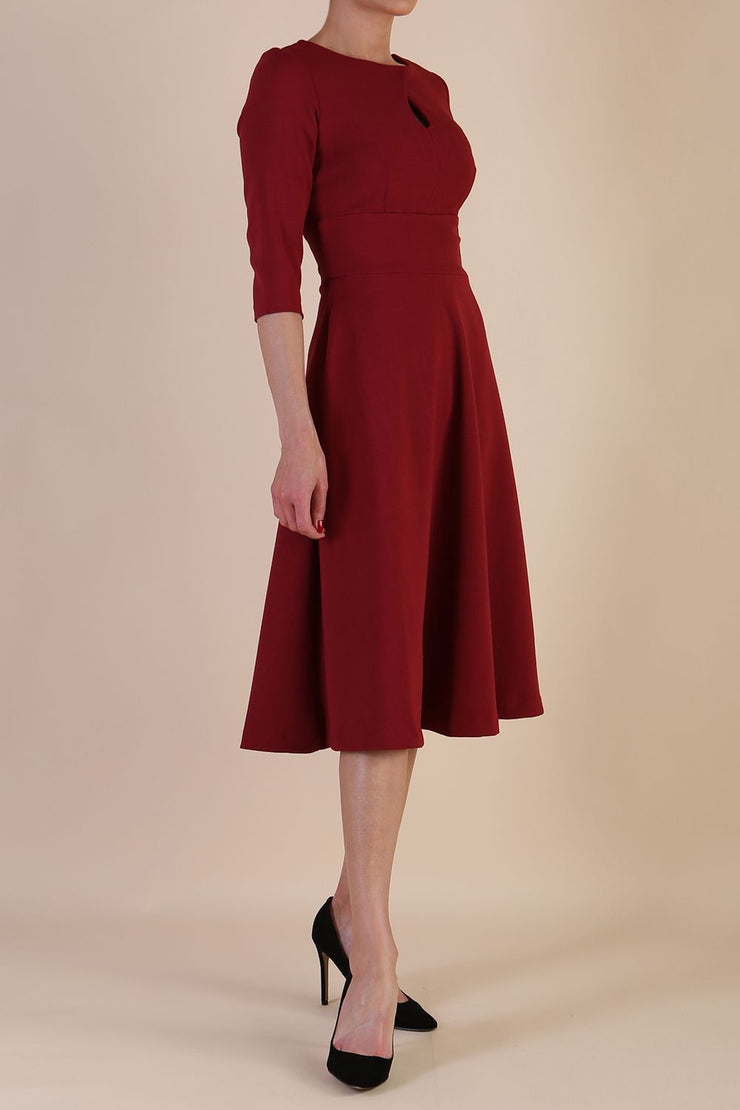 Brunette model is wearing diva catwalk casares swing dress with a keyhole neckline three quarter sleeve dress with pocket detail in Wine side front