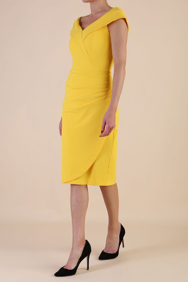 brunette model wearing diva catwalk evening pencil skirt dress sleeveless with lowered neckline and pleating on side in yellow colour front