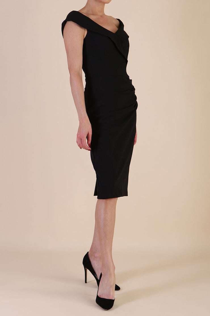 brunette model wearing diva catwalk evening pencil skirt dress sleeveless with lowered neckline and pleating on side in black colour front