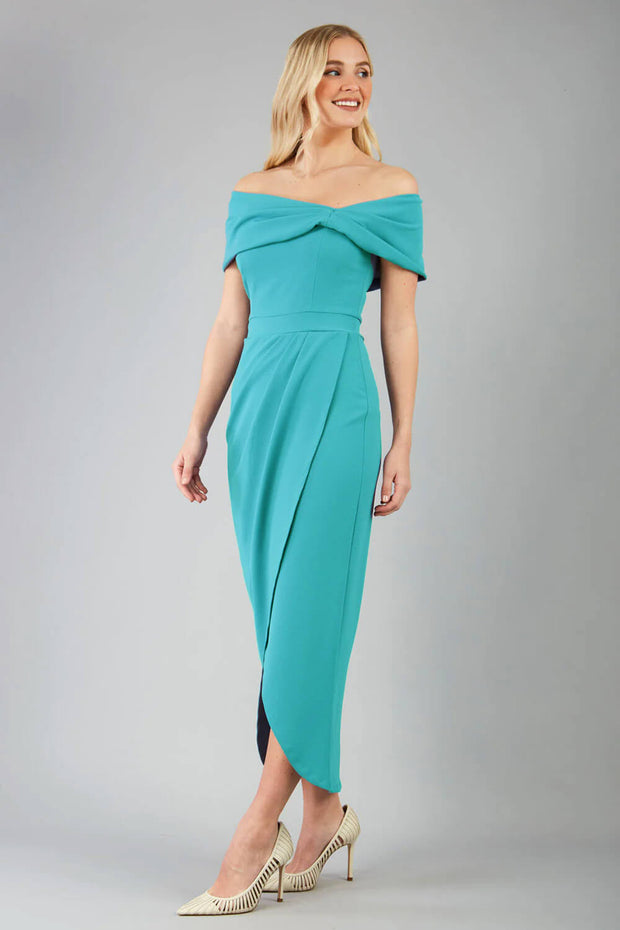 Model wearing diva catwalk vegas calf length stone blue midaxi dress with wide bardot neckline and open shoulders with a large opening at the front of the skirt with pleating coming down long skirt back
