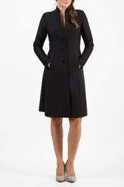 brunette model wearing diva catwalk couture fine raquella coat with buttons across the front and long sleeves with high neck and pockets in black colour front