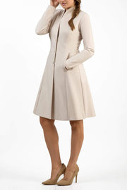 brunette model wearing diva catwalk couture fine raquella coat with buttons across the front and long sleeves with high neck and pockets in sandy cream colour front