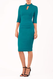 model is wearing diva catwalk pinhoe pencil dress with sleeved and high neckline with a keyhole detail in the middle and pleating across the tummy area in mosaic blue front