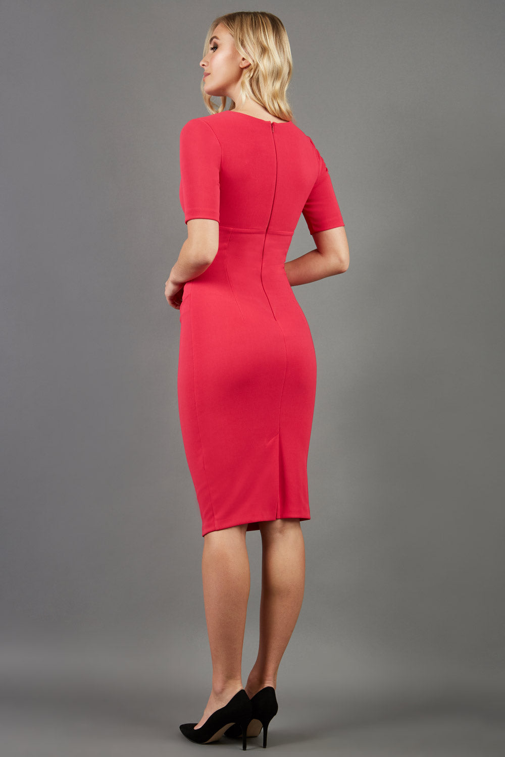 blonde model is wearing diva catwalk lydia short sleeve pencil fitted dress in paradise pink colour with rounded neckline with a slit in the middle back