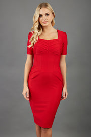blonde model wearing seed belgravia square neckline red pencil dress with short pleated sleeves and folded pleating like corset band  at the front 