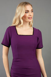 blonde model wearing seed albany contrasted pencil-skirt dress with short sleeves and pleating across the tummy with low square neckline and contrasted detail finishing in purple front