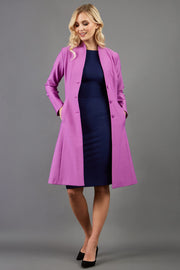 blonde model wearing diva catwalk couture fine raquella coat with buttons across the front and long sleeves with high neck and pockets in magenta mist colour front