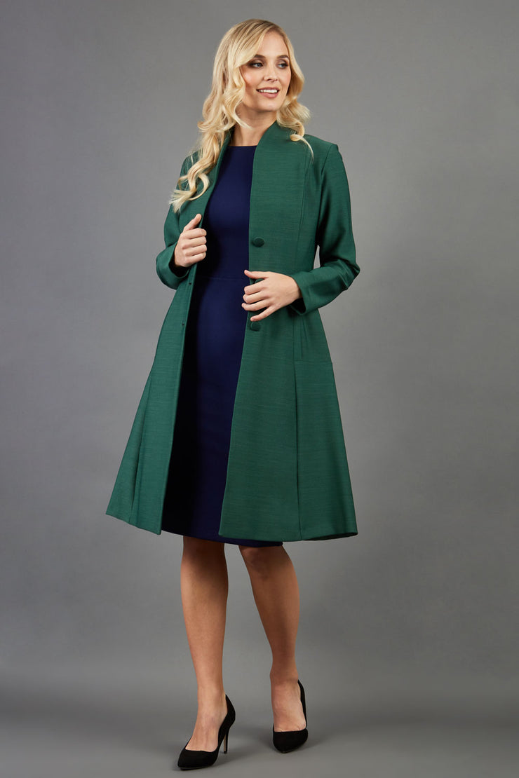 blonde model wearing diva catwalk couture fine raquella coat with buttons across the front and long sleeves with high neck and pockets in chrome green colour front