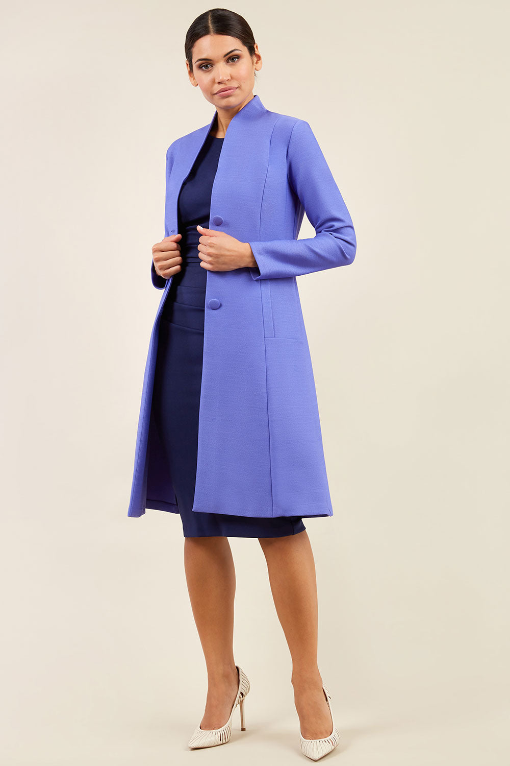 brunette model wearing diva catwalk couture fine raquella coat with buttons across the front and long sleeves with high neck and pockets in fusion indigo colour front