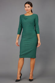 brunette model wearing diva catwalk couture althorp pencil fitted dress with sleeves and rounded neckline and bow detail at the top in chrome green colour front