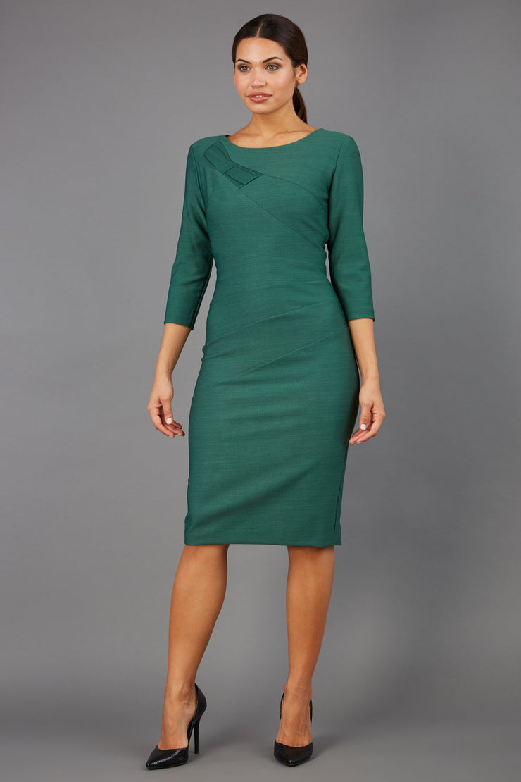 brunette model wearing diva catwalk couture althorp pencil fitted dress with sleeves and rounded neckline and bow detail at the top in chrome green colour front