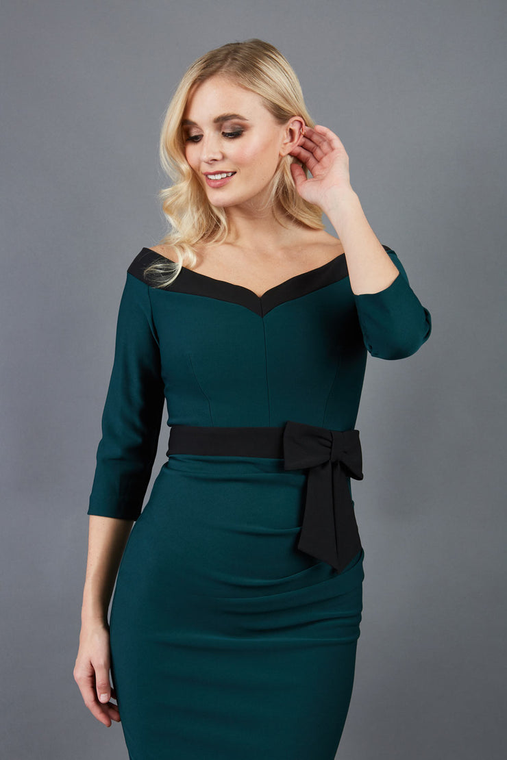 blonde model wearing diva catwalk luma pencil skirt dress with contrasting bow off shoulder with sleeves in forest green front