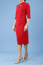 model is wearing diva catwalk pinhoe pencil dress with sleeved and high neckline with a keyhole detail in the middle and pleating across the tummy area in true red side