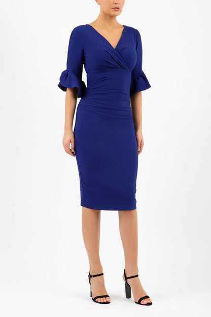 brunette model is wearing diva catwalk hollie pencil dress with frilled flute sleeve and low v-neck cut in blue front
