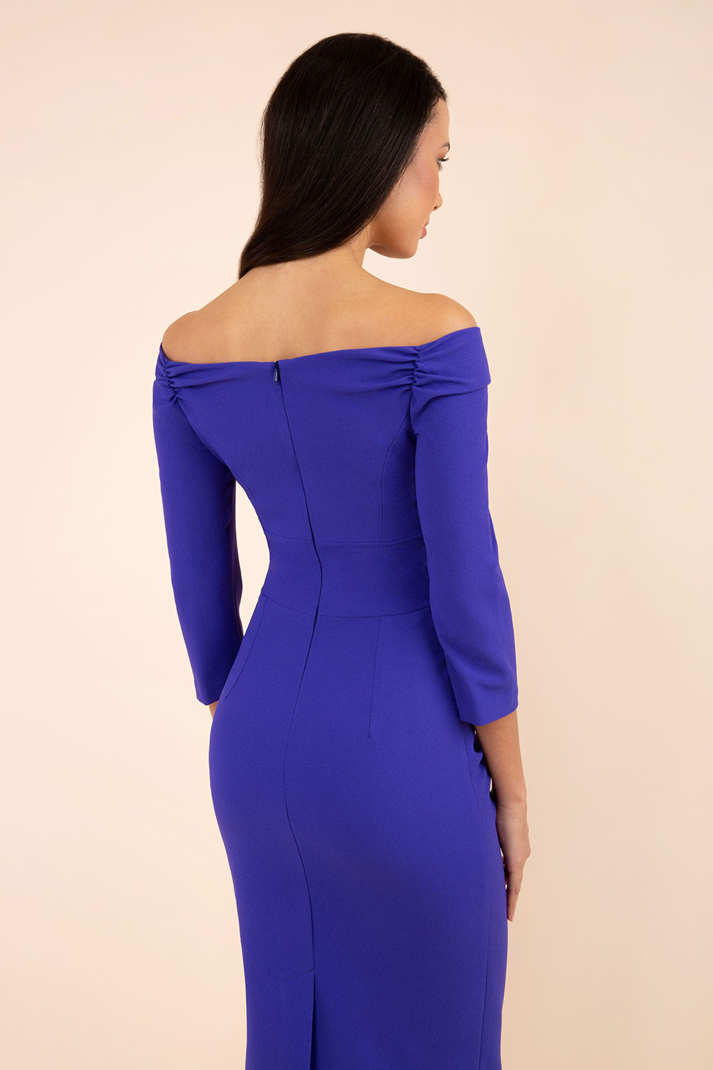 brunette model wearing diva catwalk evening pencil dress off shoulder with sleeves and pleated pencil skirt in colour indigo blue back