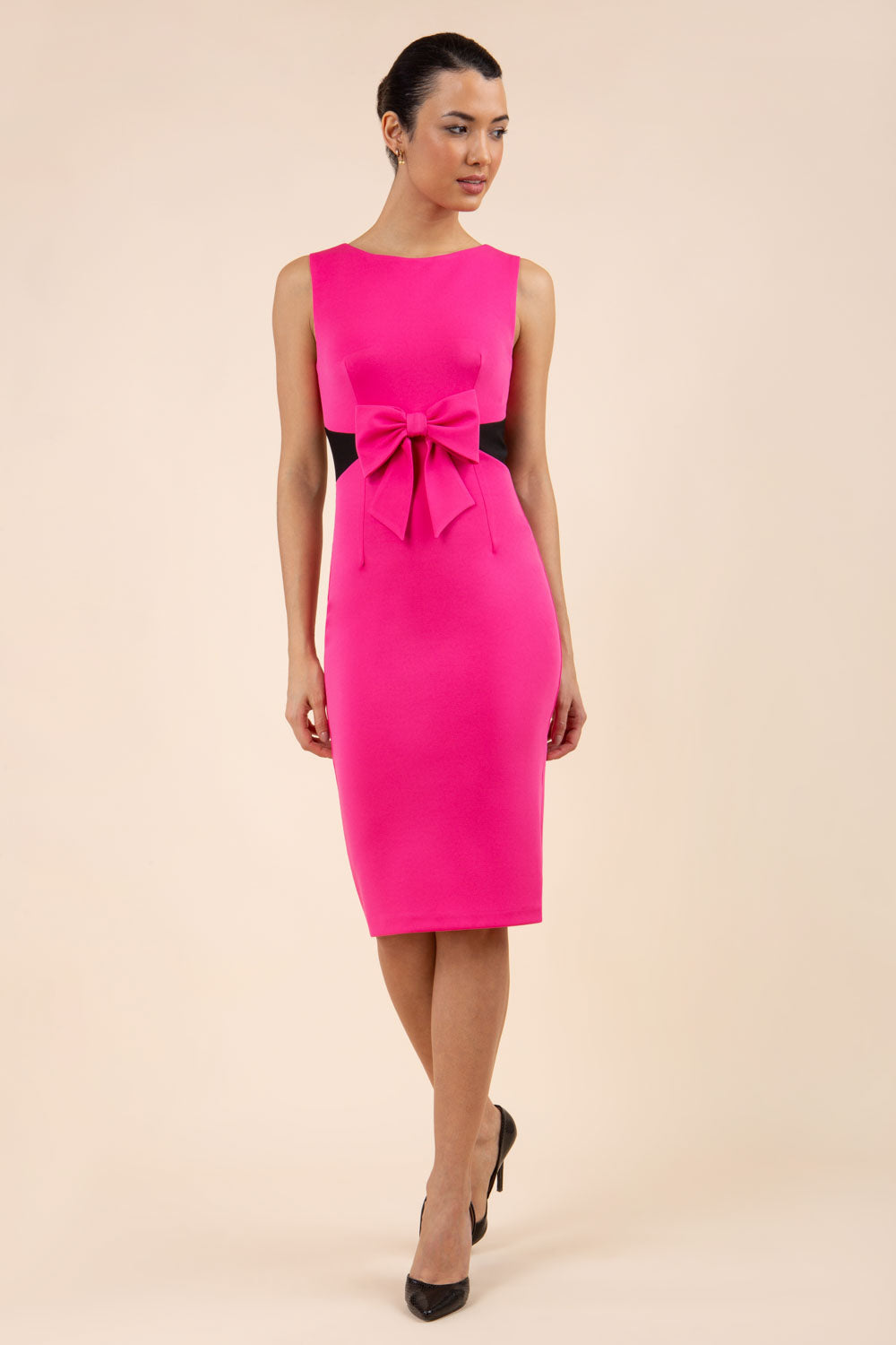 blonde model wearing Diva Catwalk Pencil sleeveless dress with rounded neckline and bow detail at the front with a contrasting black band in hibiscus pink front