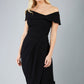 odel wearing diva catwalk vegas calf length black midaxi dress with wide bardot neckline and open shoulders with a large opening at the front of the skirt with pleating coming down long skirt front