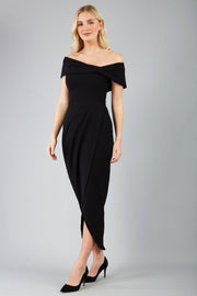 odel wearing diva catwalk vegas calf length black midaxi dress with wide bardot neckline and open shoulders with a large opening at the front of the skirt with pleating coming down long skirt front