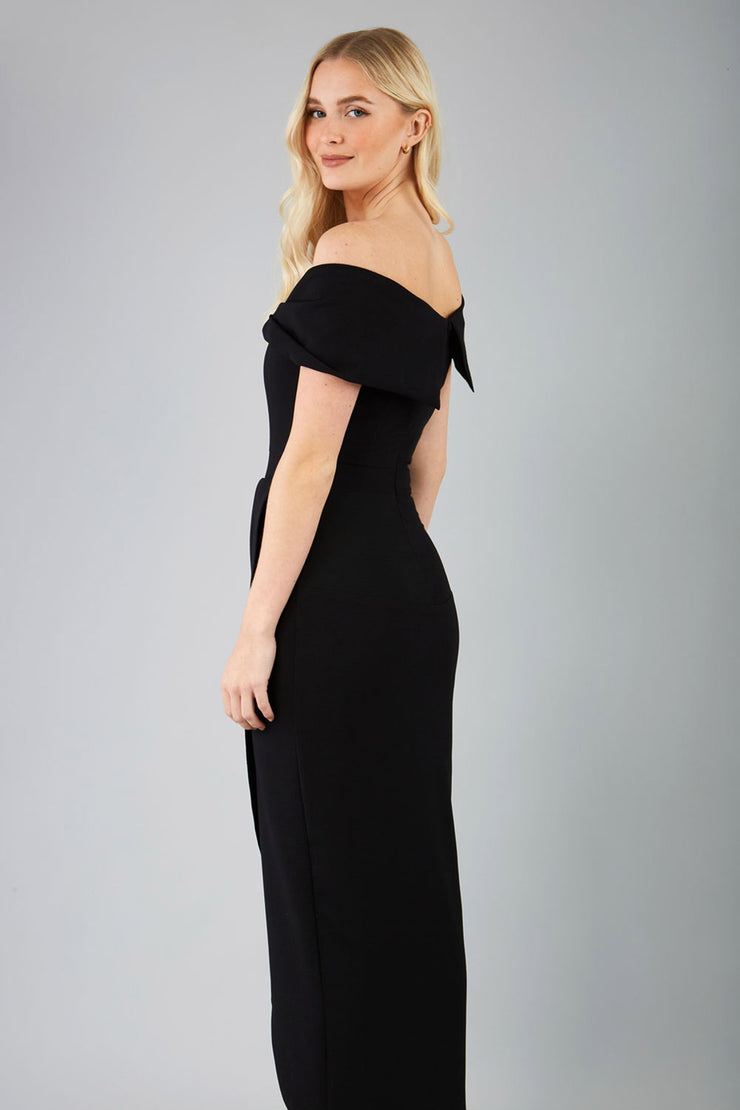 model wearing diva catwalk vegas calf length black midaxi dress with wide bardot neckline and open shoulders with a large opening at the front of the skirt with pleating coming down long skirt back