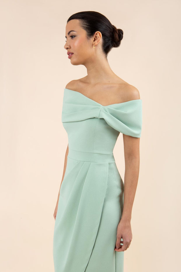 brunette model wearing diva catwalk vegas calf length pale deco green midaxi dress with wide bardot neckline and open shoulders with a large opening at the front of the skirt with pleating coming down long skirt front