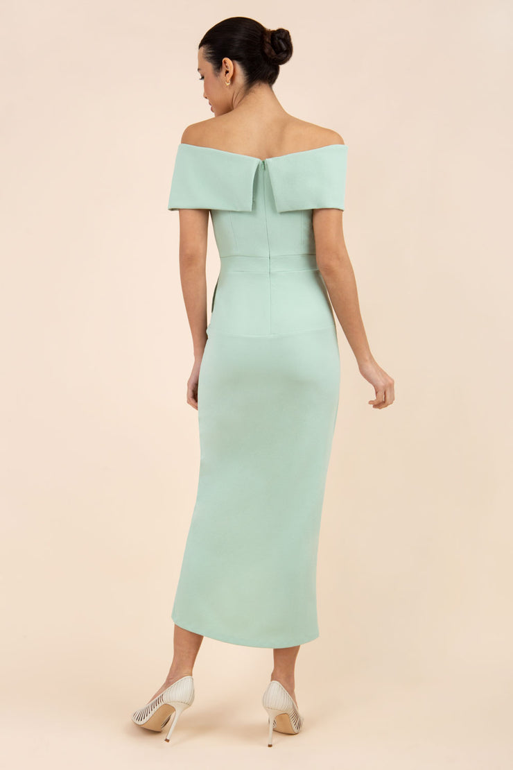 brunette model wearing diva catwalk vegas calf length pale green midaxi dress with wide bardot neckline and open shoulders with a large opening at the front of the skirt with pleating coming down long skirt back