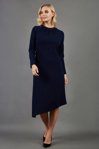 blonde model is wearing diva catwalk dartington asymmetric skirt midaxi long sleeve dress with rounded pleated neckline a-line style in navy blue front