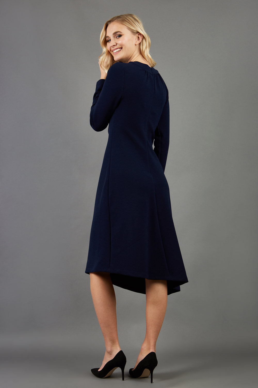 blonde model is wearing diva catwalk dartington asymmetric skirt midaxi long sleeve dress with rounded pleated neckline a-line style in navy blue back
