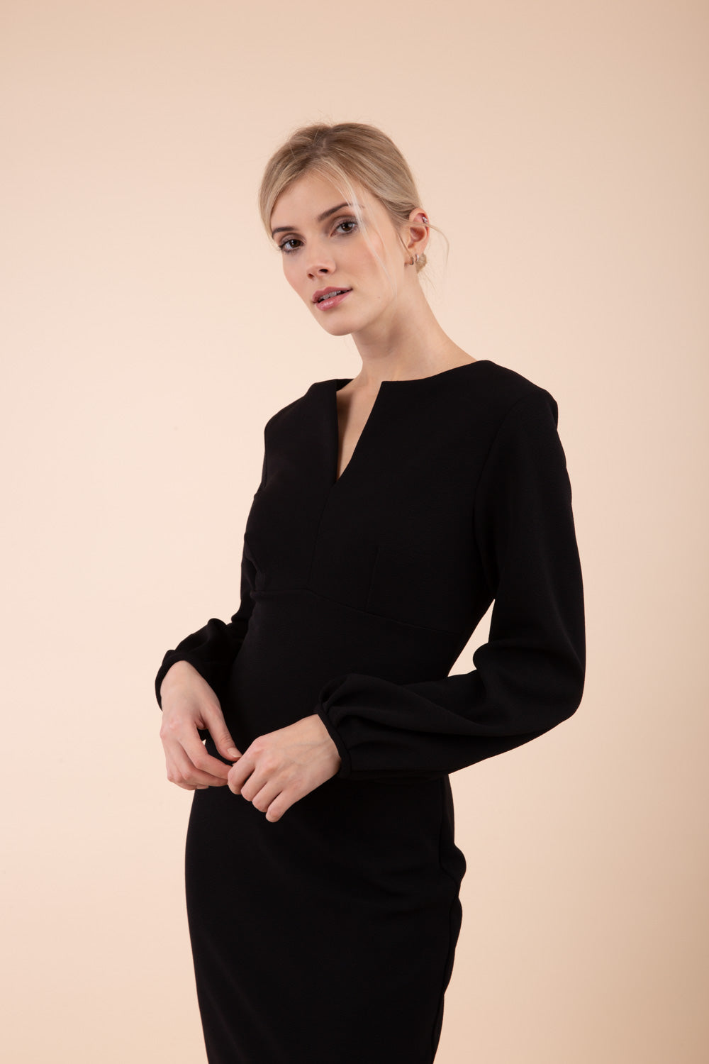 Blonde model wearing Diva Catwalk Praktica long puffed bishop sleeves knee length empire line pencil dress with round neckline with a slit cut in the middle in Black front