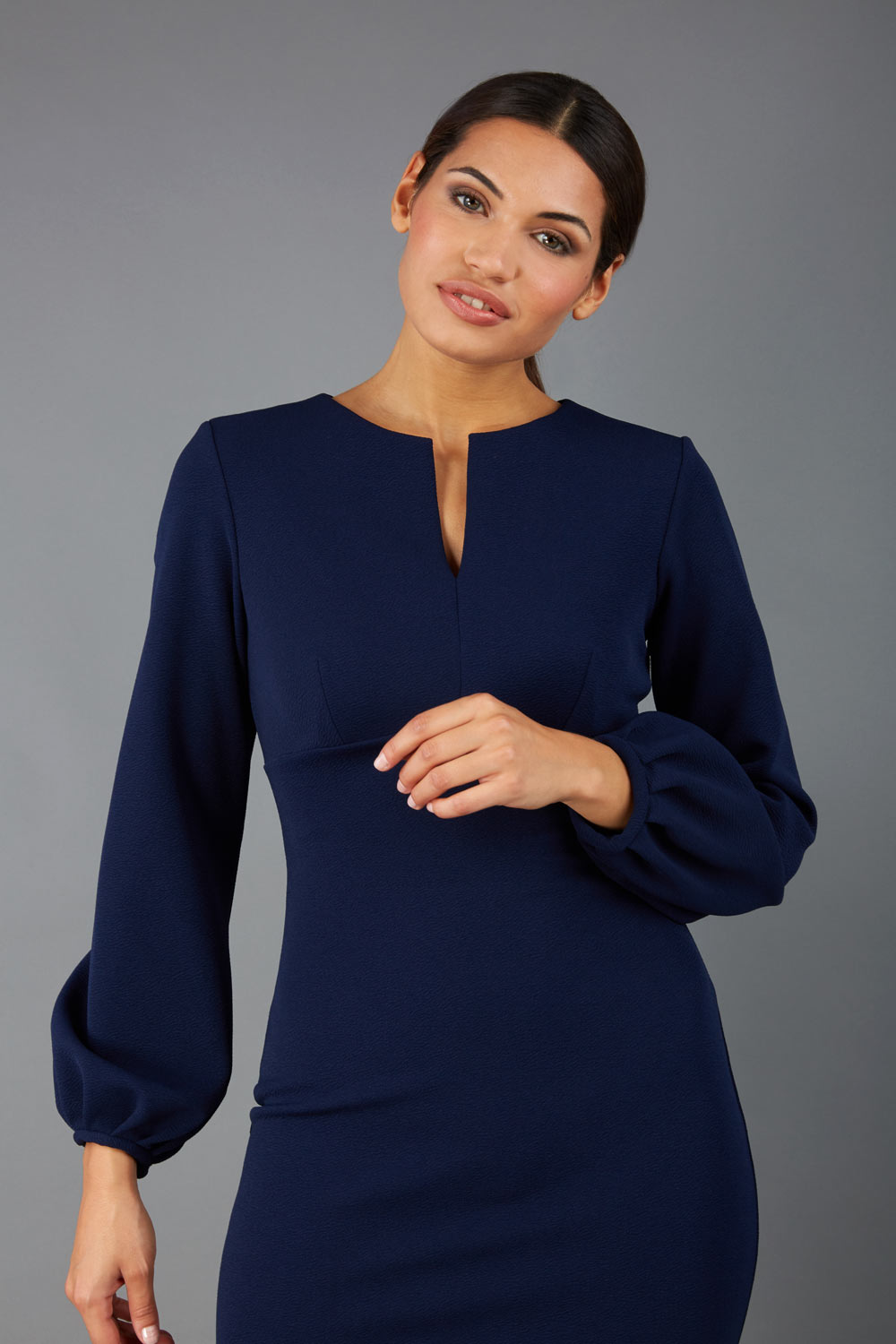 brunette model wearing Diva Catwalk Praktica long puffed bishop sleeves knee length empire line pencil dress with round neckline with a slit cut in the middle in navy front