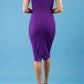 brunette model wearing diva catwalk lydia sleeveless pencil flattering fitted plain dress with split neckline and pleating across the body passion purple back