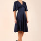 brunette model wearing diva catwalk cambrian satin swing dress with bell short sleeve wide asymmetric waistband and pleating under bust and low v-neckline in navy front