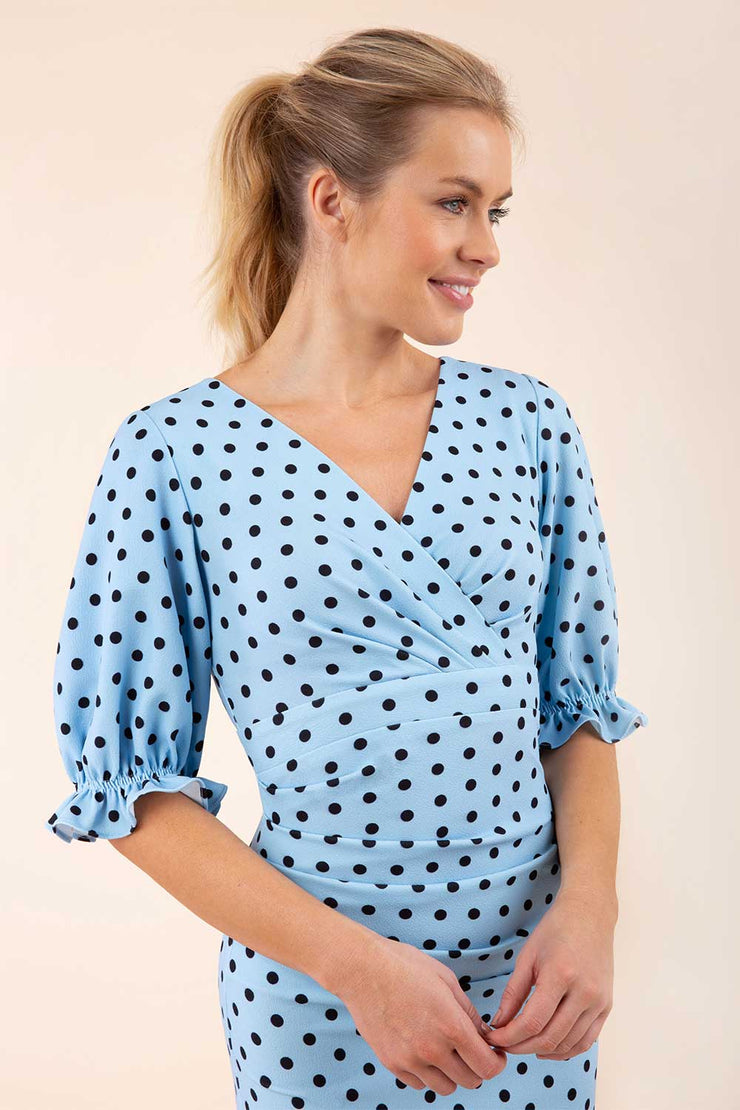 Blonde model wearing Diva Catwalk Palacio Pencil dress v neckline and pleating across the tummy with puffed short sleeves in blue polka dot front