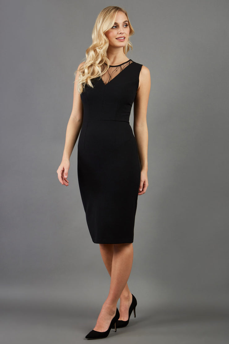 blonde model wearing diva catwalk pastiche pencil fitted sleeveless dress v-neckline with lace overlay in black front